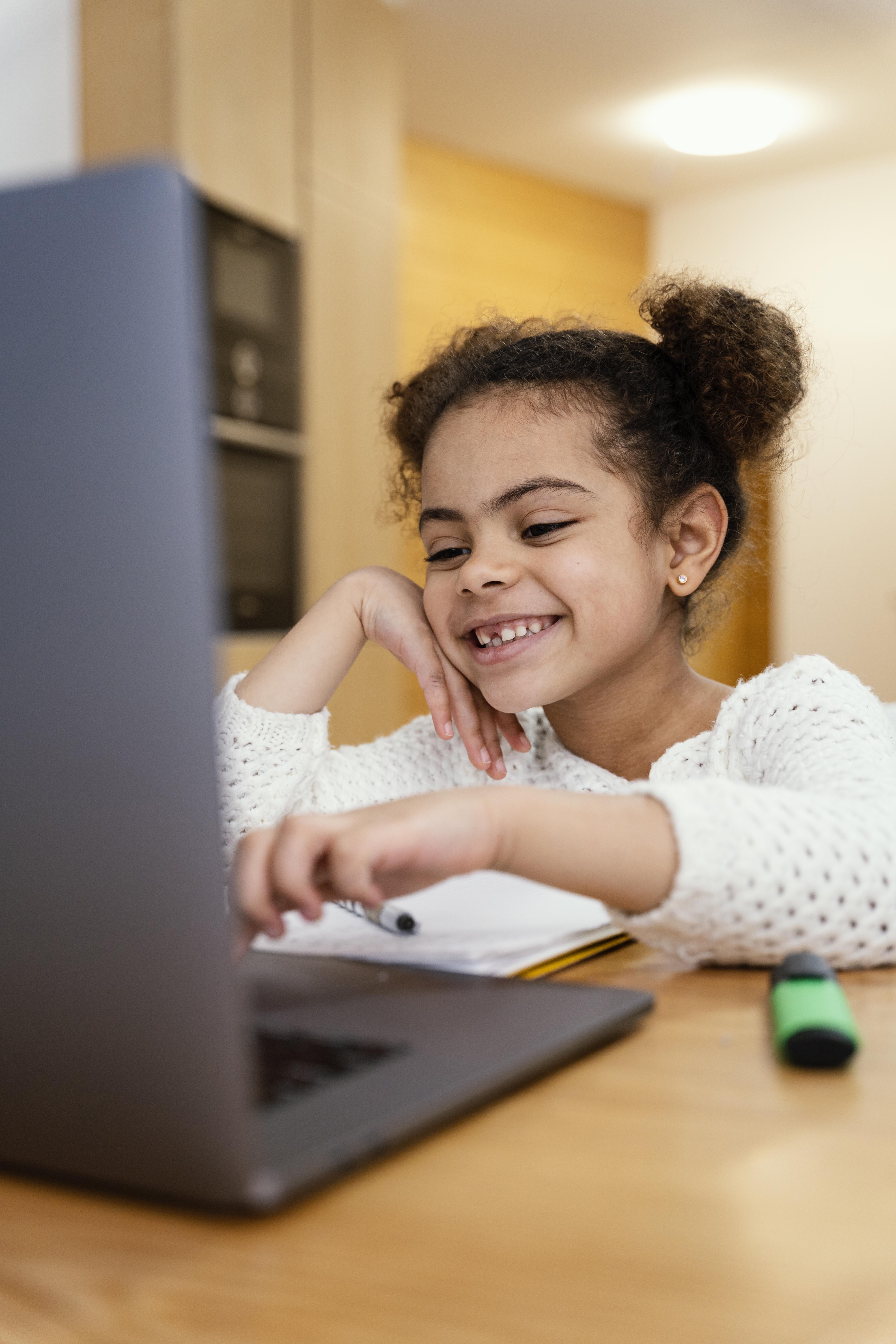 Imagem de uma criança sorridente usando um laptop em ambiente doméstico.
